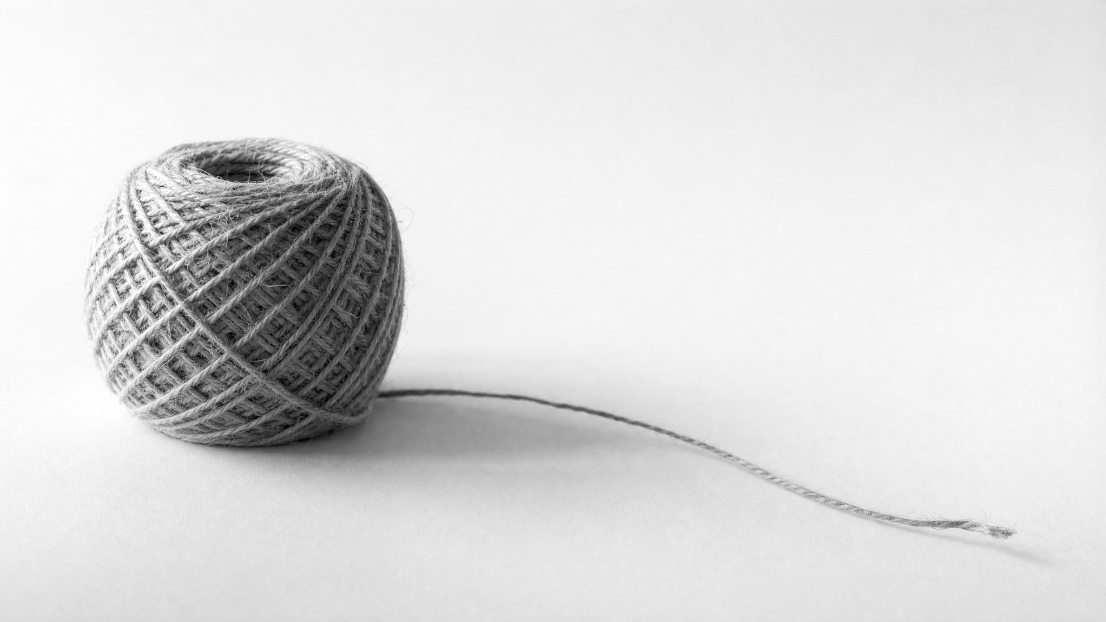 A tightly wound ball of twine with one loose end trailing across a white surface